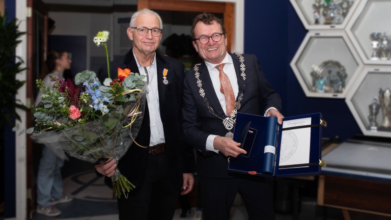 Twee mannen poseren samen, de een met een boeket bloemen en de ander met een medaille.