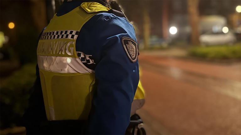 Politieagent in uniform op straat 's avonds, met reflecterend vest en embleem op de arm.