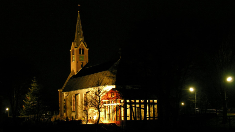 Verlichte kerk in de nacht met omringende bomen en straatverlichting.