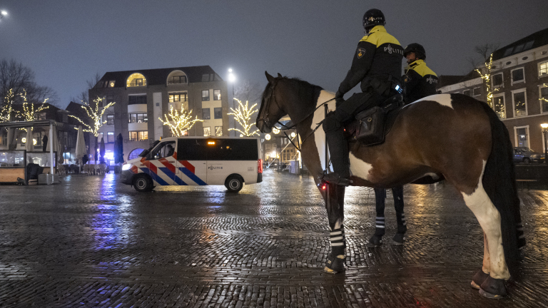 Politie te paard en politiebusje op een verlichte plein in de avond.