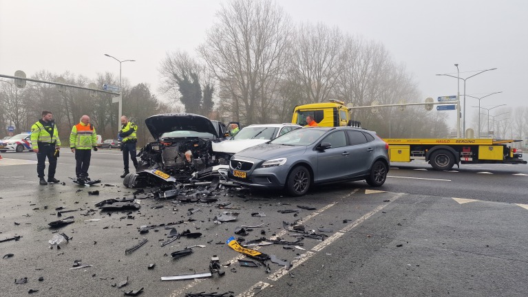 Twee auto's betrokken bij een botsing op een kruispunt, omringd door politie en bergingsvoertuigen.