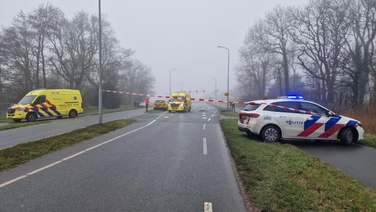 Politie en ambulances blokkeren een weg met rood-wit lint op een mistige dag.