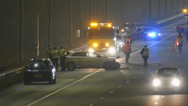 Nachtelijke verkeersongeluk op snelweg met beschadigde auto, hulpdiensten en bergingsvoertuig.