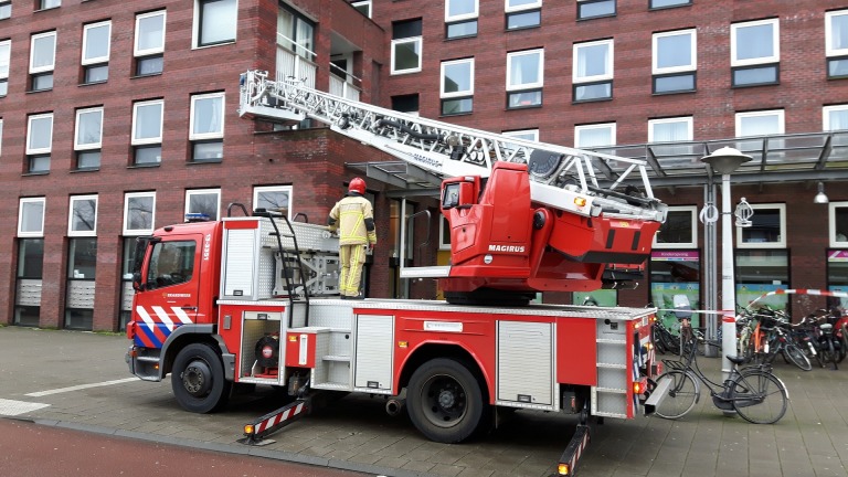 Brandweerwagen met ladder bij een bakstenen gebouw, met een brandweerman op het voertuig.