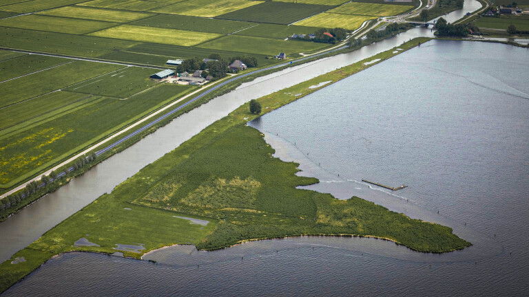 Luchtfoto van een polderlandschap met kanalen en een groot waterlichaam, omgeven door agrarisch gebied en wegen.