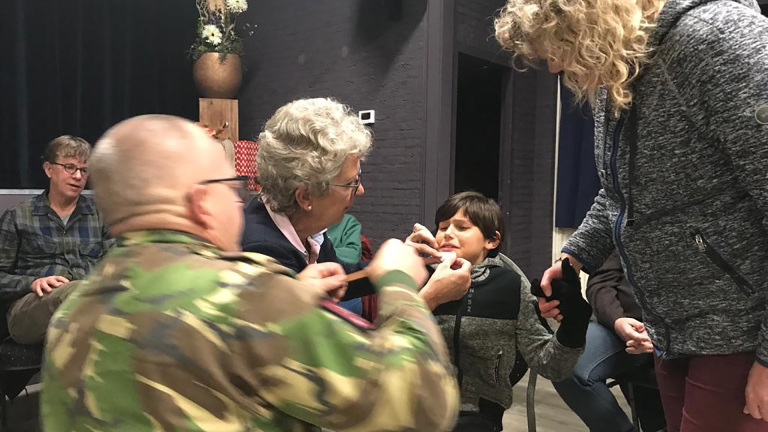 Een jongen krijgt een EHBO-behandeling van volwassenen in een kamer met andere mensen.