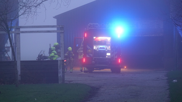 Brandweervoertuig met zwaailichten en brandweerlieden bij een gebouw in mistige omstandigheden.