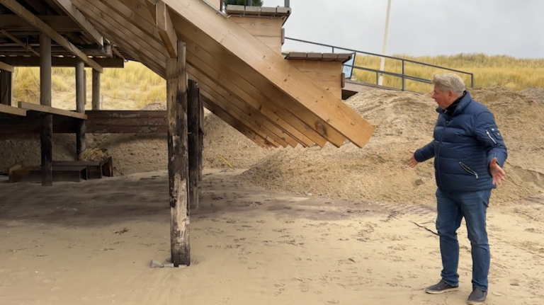 Man naast een houten strandstructuur, met zandduinen op de achtergrond.