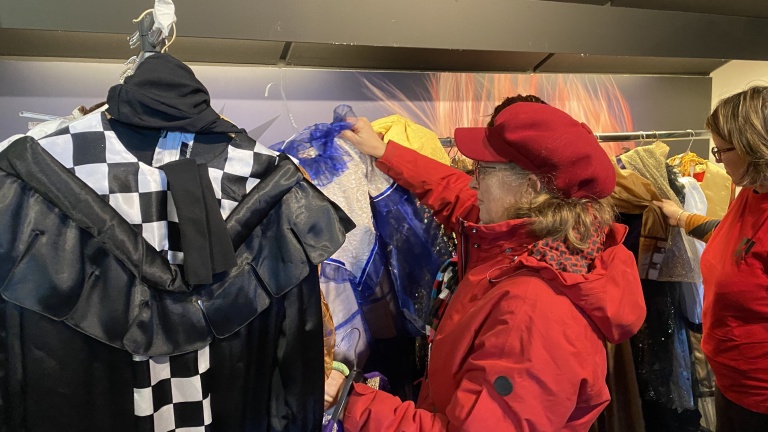 Twee vrouwen zoeken tussen kleding op een kledingrek, waaronder een zwart-wit geruit kostuum.