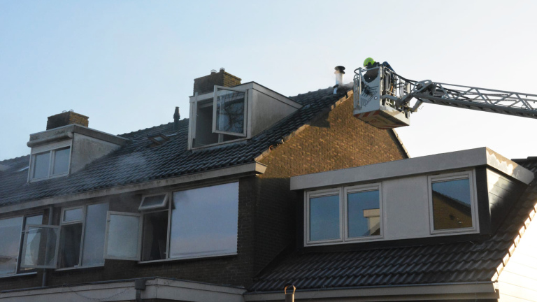 Brandweerman in hoogwerker blust schoorsteenbrand op dak van rijtjeshuis.