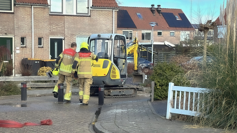 Twee brandweerlieden lopen naar een kleine graafmachine in een woonwijk.