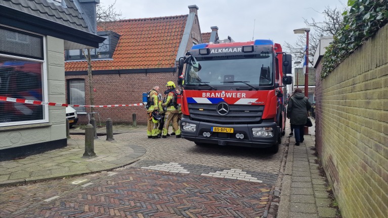 Brandweerwagen in smal straatje met brandweermannen bij rood-wit afzetlint.