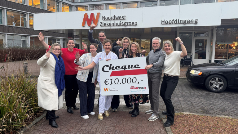 Groep mensen houdt een cheque van €10.000,- vast voor de Noordwest Ziekenhuisgroep, buiten bij de hoofdingang van het ziekenhuis.