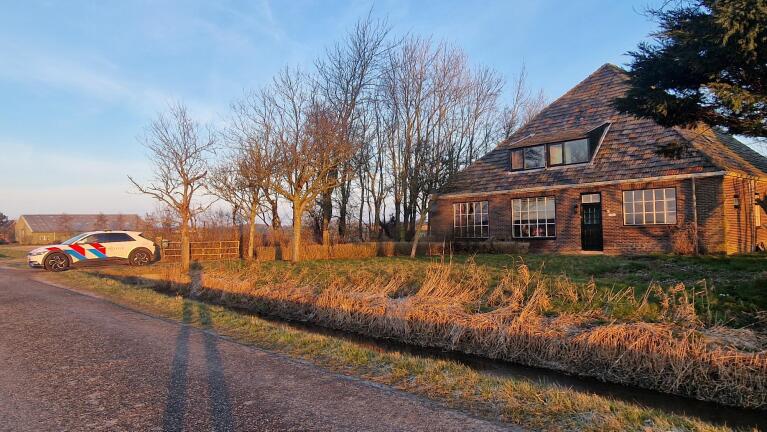 Een politieauto staat geparkeerd naast een huis op een plattelandsweg bij zonsondergang.