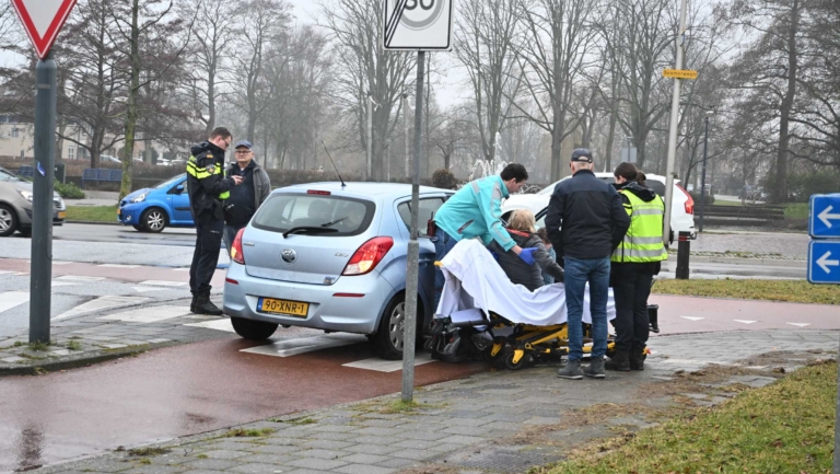 Een ongeluksscène met een auto en een brancard, omringd door hulpverleners en politieagenten.