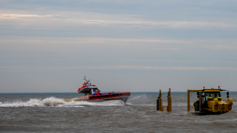 Reddingsboot op zee met grote golven en een voertuig op het strand.