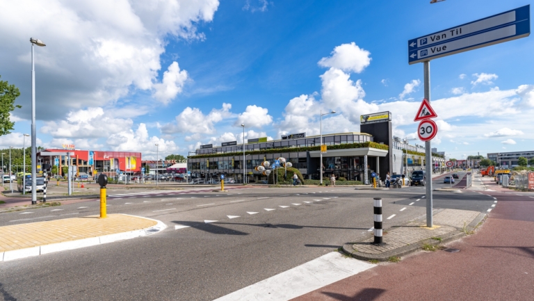 Winkelgebied met gebouwen, wegwijzers en verkeersborden onder een blauwe lucht met wolken.