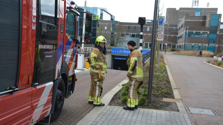 Brandweerlieden in uniform staan naast een brandweerwagen bij een ondergrondse parkeergarage.