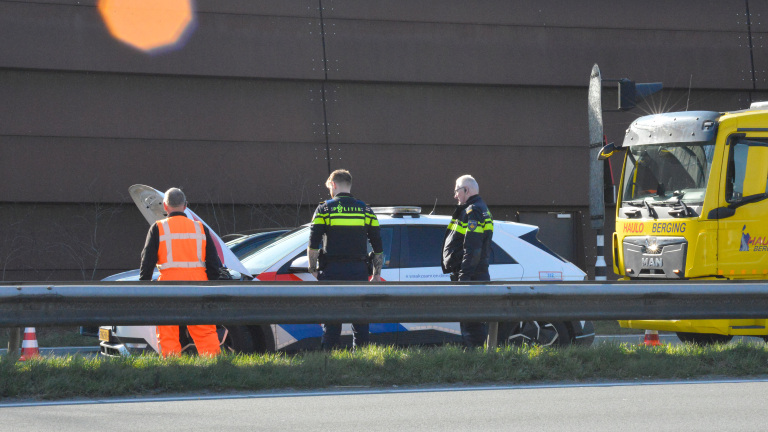 Drie mannen naast een politieauto met geopende motorkap op de snelweg, naast een bergingsvoertuig.