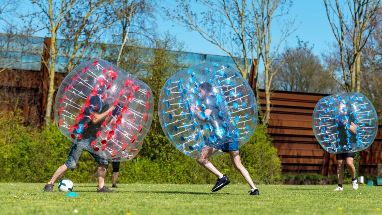 Mensen spelen bubbelvoetbal op een grasveld met opblaasbare ballen.