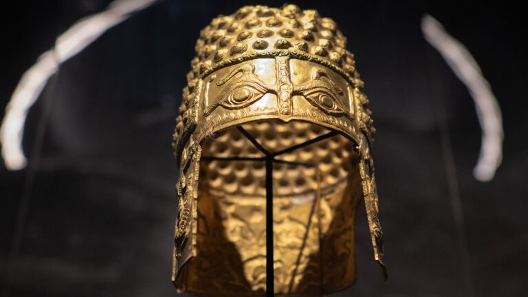 Gouden antieke helm met gedetailleerde decoraties en een patroon van verhoogde stippen.