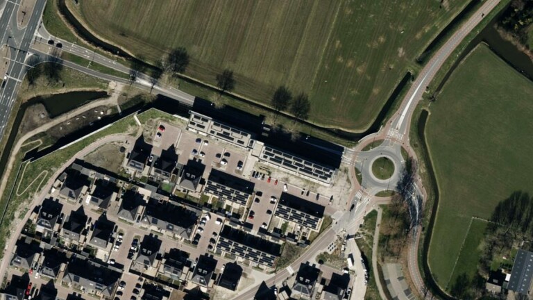 Luchtfoto van een woonwijk met huizenblokken, parkeerplaatsen, groenvoorzieningen en een rotonde.