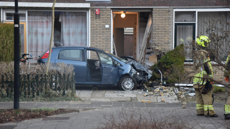 Auto gecrasht tegen gevel van een rijtjeshuis; brandweerlieden aanwezig.