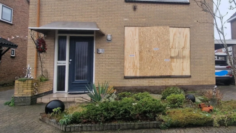 Twee-onder-een-kapwoning met een dichtgetimmerd raam op de begane grond, verzorgde voortuin en blauwe deur.