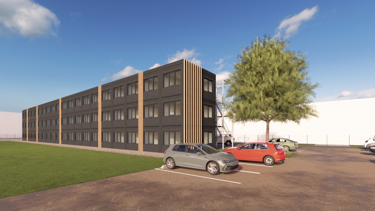 Een modern, donkergekleurde drie verdiepingen hoge kantoorgebouw met houten verticale details, omringd door een parkeerplaats met meerdere auto's en een groene boom naast het gebouw. De lucht is helder met enkele wolken.