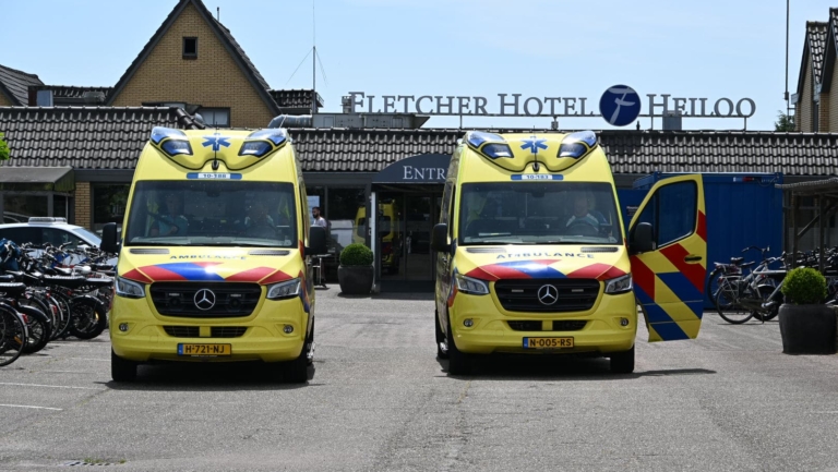 Twee gele ambulances geparkeerd voor Fletcher Hotel Heiloo, met een van de deuren van de rechterambulance open, en fietsen aan de zijkant van de parkeerplaats.