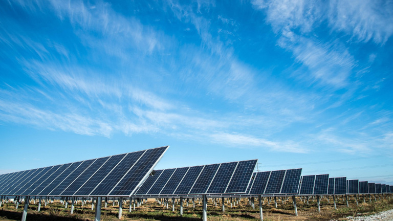 Een veld met rijen zonnepanelen onder een heldere blauwe hemel.
