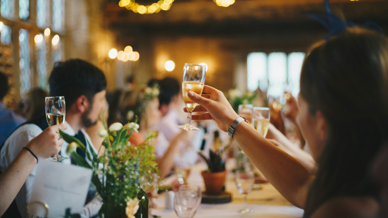 Groep mensen tilt glazen champagne op tijdens een feestelijke toast in een sfeervol ingerichte zaal.