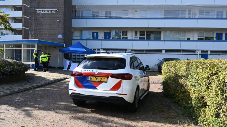 Een politieauto en drie agenten voor een gebouw genaamd 'Molenzicht'. Er is een blauwe tent opgezet bij de ingang van het gebouw.