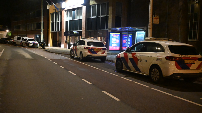 Drie politieauto's geparkeerd langs een straat in de nacht, met een gebouw en een bushalte op de achtergrond.
