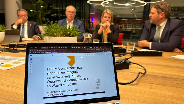 Vergaderruimte met laptop op tafel waarop een presentatie over PRISMA-onderzoek te zien is; op de achtergrond zitten vier mensen aan de vergadertafel.