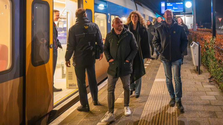 Mensen stappen 's avonds in een gele en blauwe trein op een station in Nederland.