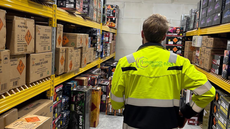 Persoon in gele jas inspecteert dozen met gevaarsetiketten in een opslagruimte.