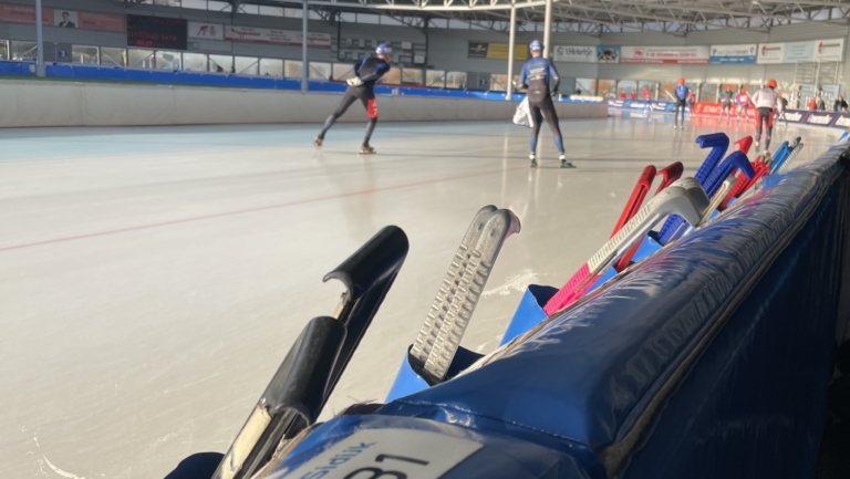 Schaatsbaan met schaatsers die aan het trainen zijn, schaatsbeschermers liggen langs de rand van de baan.