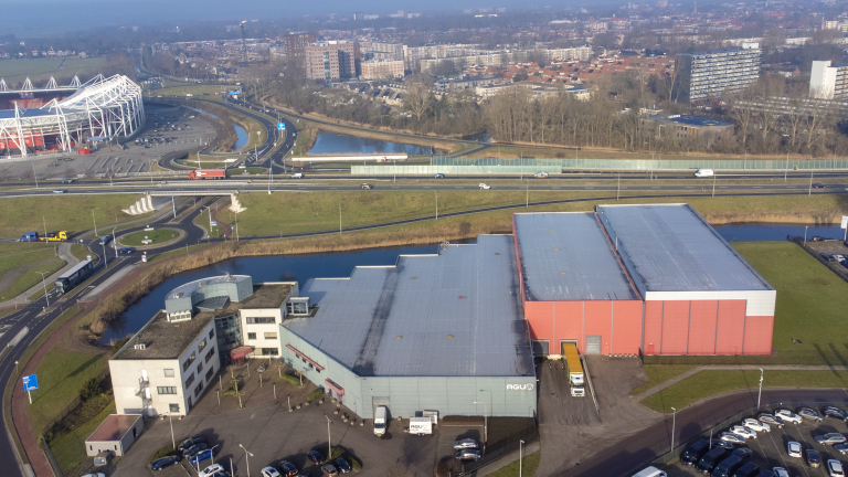 Industriegebouwen en wegen met een stadion op de achtergrond en stedelijke bebouwing verderop.