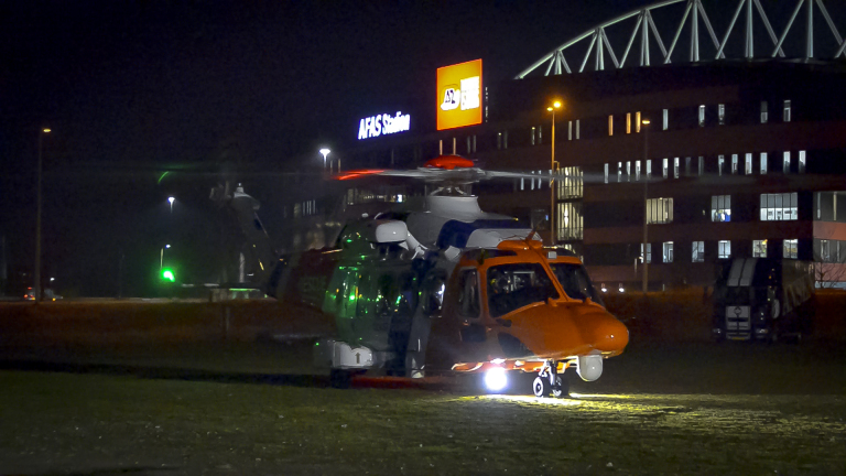 Een helikopter staat geparkeerd voor het AFAS Stadion in de avond, met lichten aan.