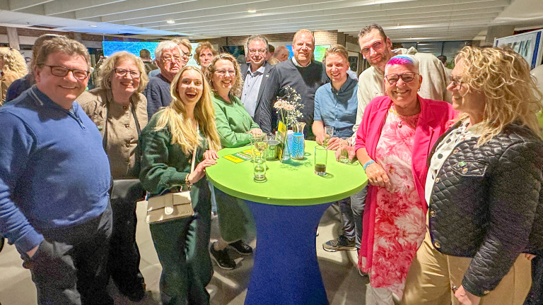 Groep mensen gezellig samen rond een hoge tafel met drankjes in een binnenruimte.