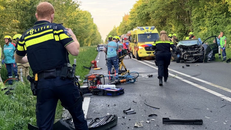 Politieagenten, medische hulpverleners en een ambulance bij een verkeersongeval met een zwaar beschadigde auto op een weg.