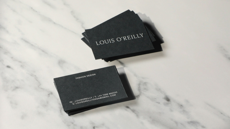 Stapels zwarte visitekaartjes met de tekst "LOUIS O'REILLY" en contactinformatie, op een marmeren ondergrond.