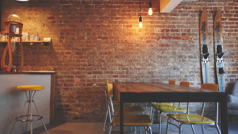 Stijlvolle ruimte met bakstenen muur, houten tafel, gele stoelen en ski's als decoratie aan de muur.