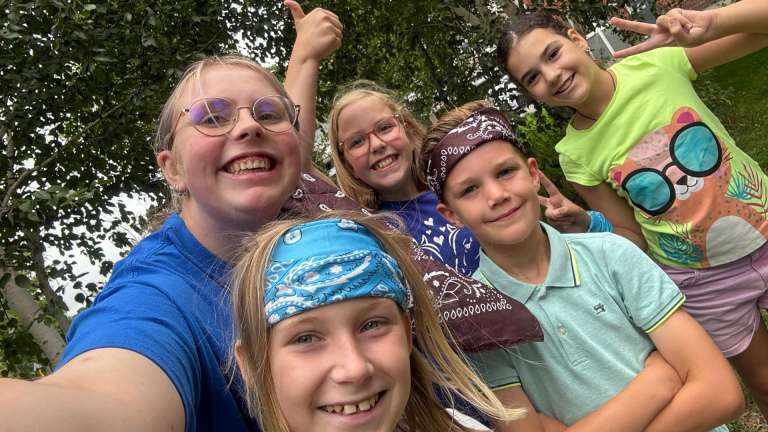 Groep kinderen die buiten lachend poseren, sommigen met hoofdbanden en gekleurde kleding.