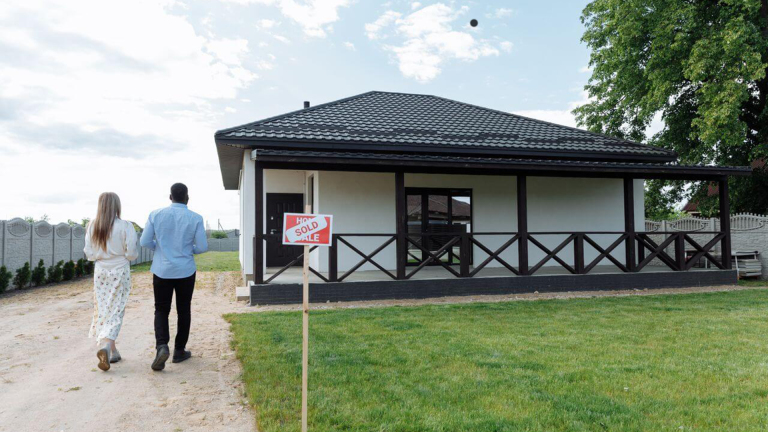 Een koppel loopt naar een huis met een "Verkocht" bord in de voortuin.