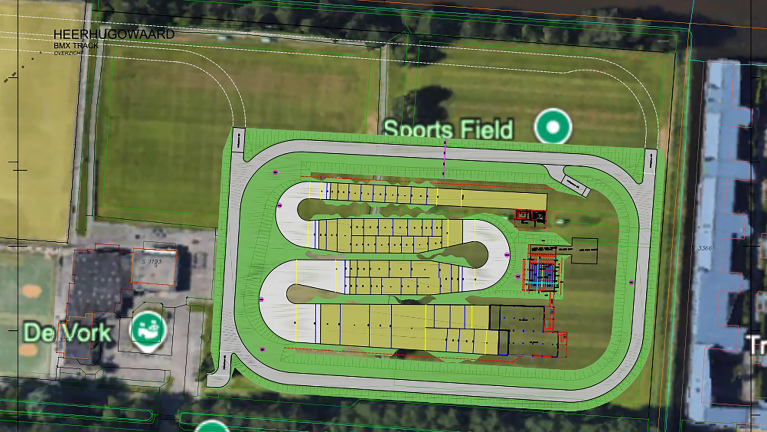 Luchtfoto van een BMX-baan in Heerhugowaard met verschillende bochten en een sportveld naast "De Vork"-gebouw.