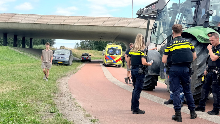Politie bij een grote tractor op een fietspad onder een viaduct, met een ambulance en voertuigen op de achtergrond
