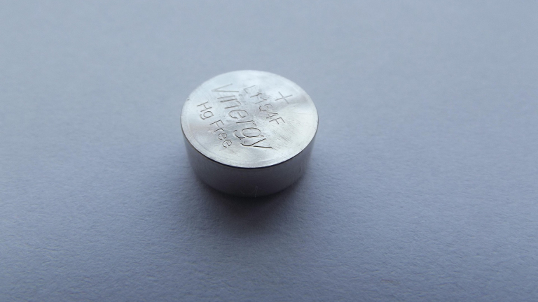 Close-up van een zilverkleurige knoopcelbatterij op een grijze ondergrond, met opdruk “Vinnic” en plus-teken