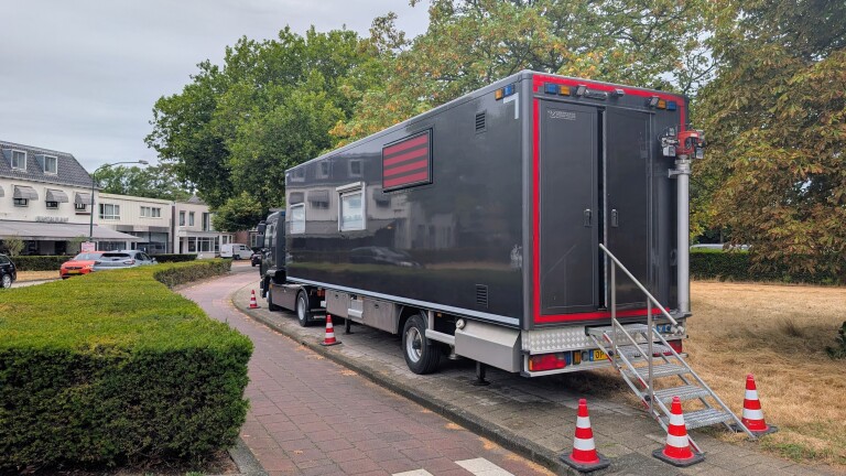 Grote zwarte vrachtwagen met trap en afzetkegels geparkeerd langs de weg bij bomen en gebouwen